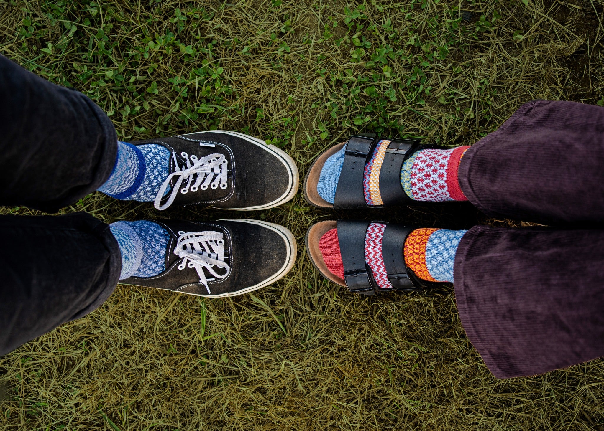 Looking down at the shoes of two people who are standing in the grass looking face to face at each other. 