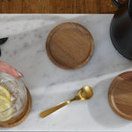 A marble cutting board sits on top of a wooden table. On the cutting board is a coffee carafe, water glass, golden spoon and some wooden coasters. The linked collection contains all of the home and kitchenware products offered by The Good Planet Company. 