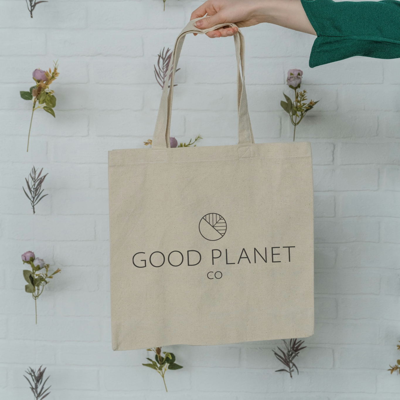 A hand holding out a organic cotton tote bag printed with the Good Planet Logo in the center of the bag. 