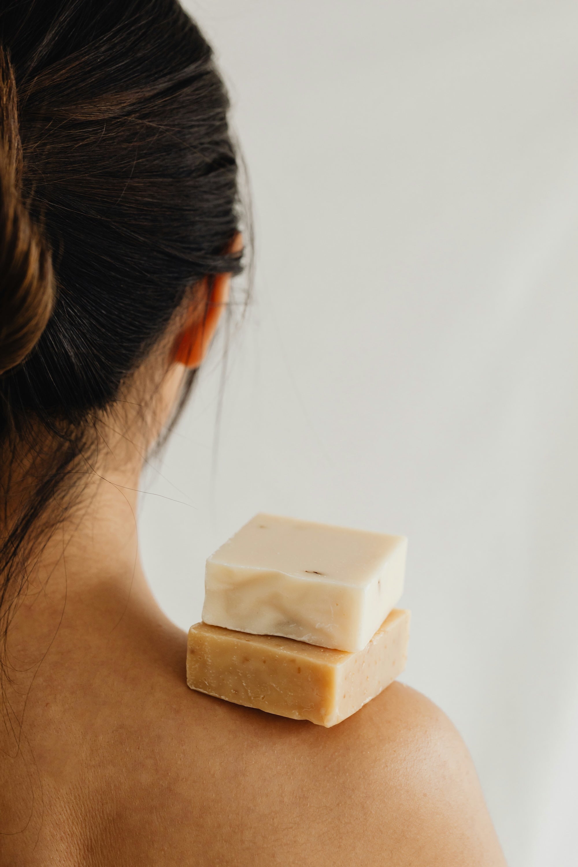 Two bars of The Good Planet's handmade organic soap are stacked on top of a woman's bare right shoulder. 