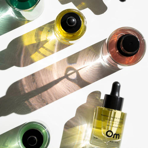 Looking down at four bottles of Om Organics products that sit on a white table top lit up by the sun. 